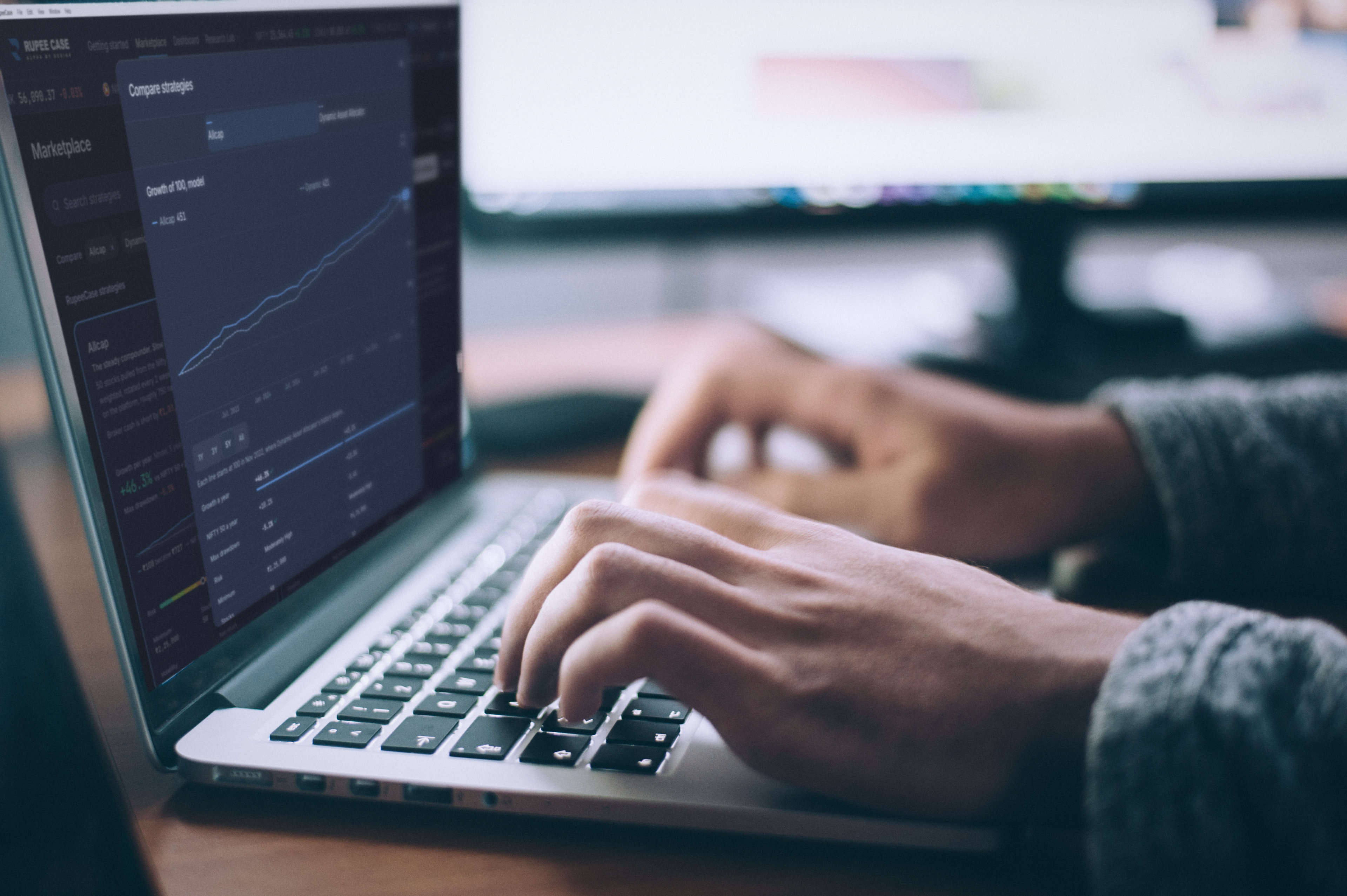 Hands typing on a laptop in an office, the screen showing the RupeeCase compare view of Allcap against Dynamic Asset Allocator, growth of 100, model