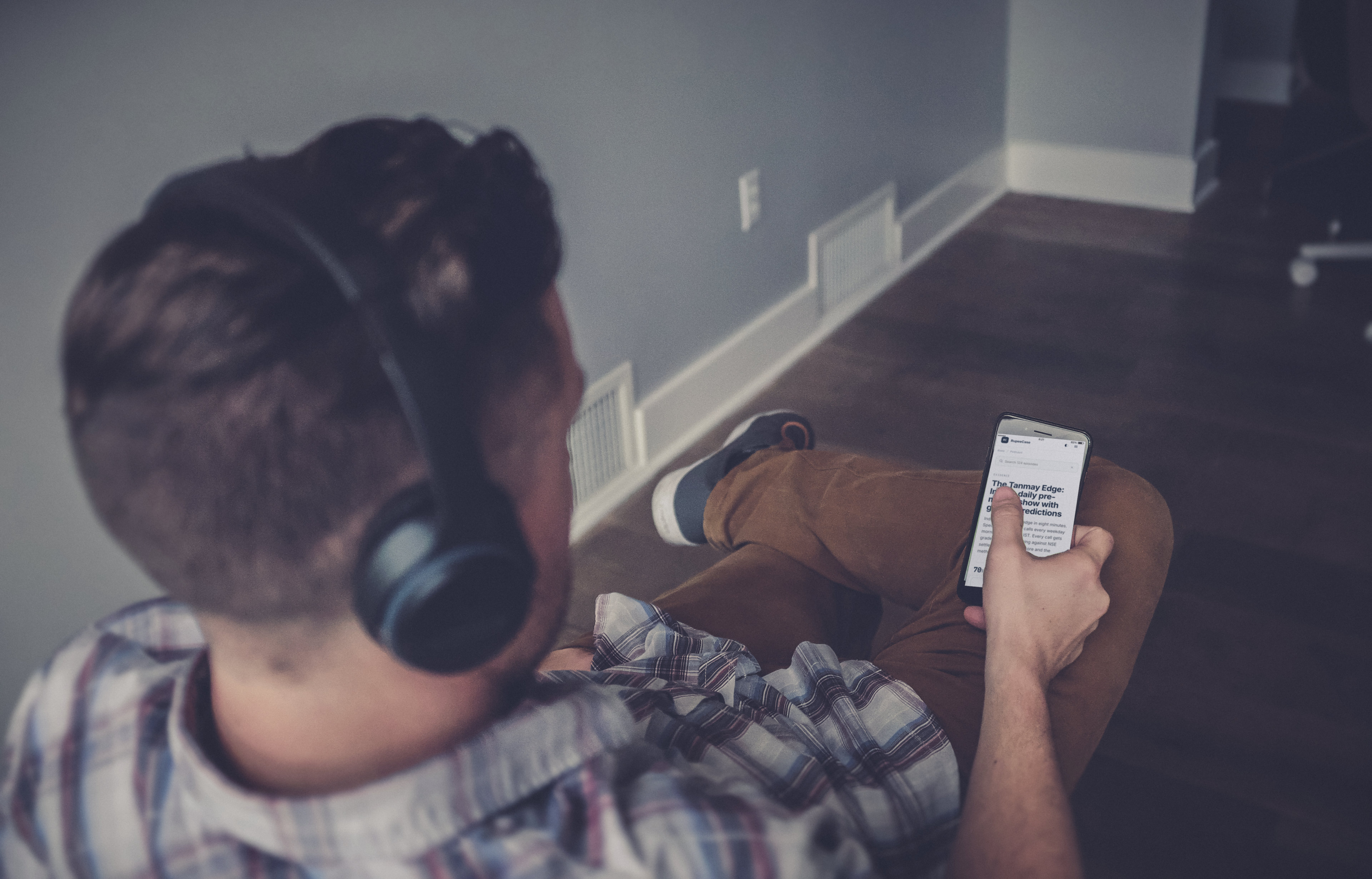 A listener in headphones sitting on the floor and scrolling the RupeeCase podcast page for The Tanmay Edge
